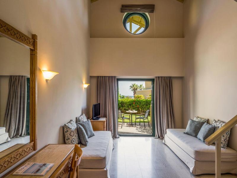 Cozy hotel room with sofas, a wooden dresser, and a balcony view of greenery.