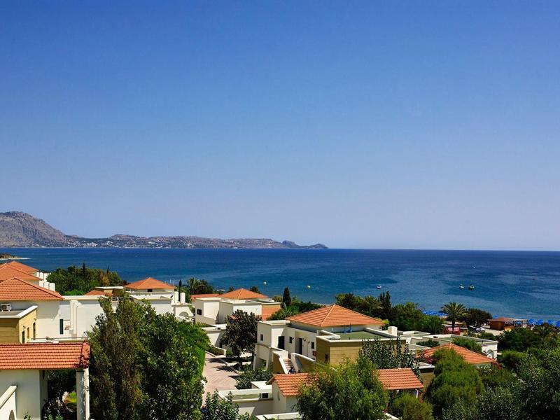 Coastal village with red-roofed houses and blue sea under clear sky.