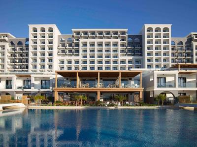 Grande hotel con più balconi e una piscina in primo piano sotto un cielo limpido.
