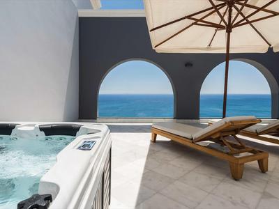 Terrazza con vasca idromassaggio, due lettini e vista sul mare attraverso due finestre ad arco.