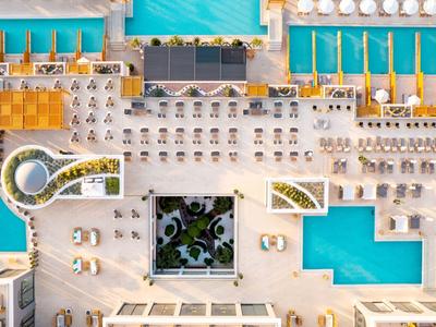 Vogelperspektive eines modernen Hotels mit Pool und Liegestühlen im Sonnenschein.