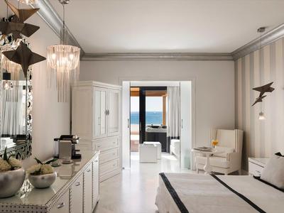 Camera d'hotel luminosa con tonalità neutre, zona salotto e vista sul mare.