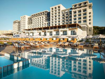 Ein großes Hotel mit mehreren Stockwerken spiegelt sich in einem blauen Pool mit Sonnenliegen wider.