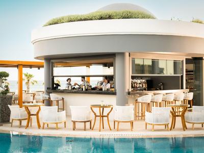 Moderner Hotelbarbereich mit Rattanmöbeln und Pool in entspannter Atmosphäre.
