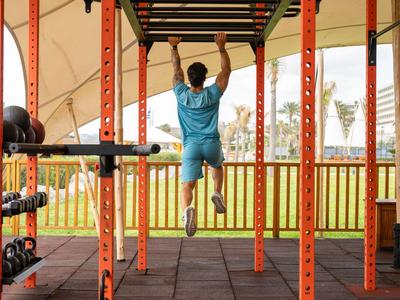 Mann trainiert an orangefarbener Klimmzugstange im offenen Fitnessbereich bei Hotel oder Resort.