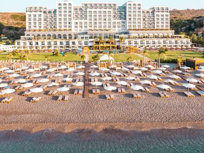 Großes weißes Hotel am Strand mit vielen Sonnenschirmen und Liegen vor dem Wasser.
