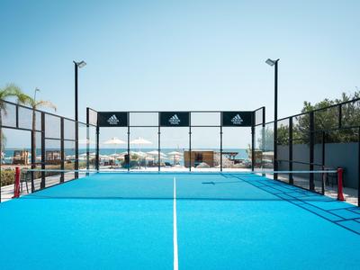 Blauer Padelplatz mit Netz und Umzäunung bei sonnigem Himmel in einem Hotel.