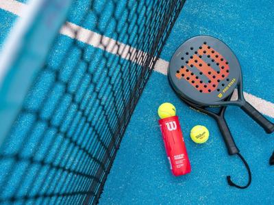 Padelschläger, Tennisbälle und Ballröhre auf blauem Platz neben Netz liegend.