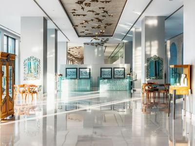 Heller Hotellobby mit spiegelnden Böden, moderner Rezeption und dekorativer Deckenmalerei.