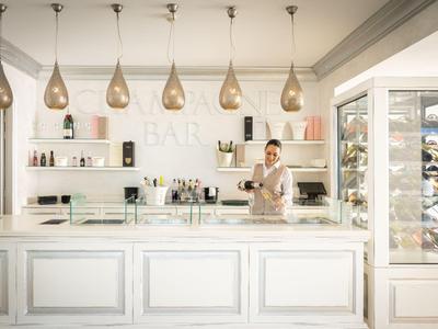 Ein moderner Hotelbarbereich mit elegantem weißen Tresen, Glashängelampen und einem Barkeeper.