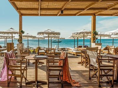 Überdachte Strandbar mit Holzstühlen und weißen Sonnenschirmen am Meer.