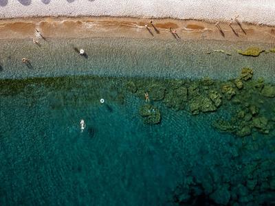 Strand mit klarem Wasser und wenigen Menschen, Felsen am Meeresgrund sichtbar.