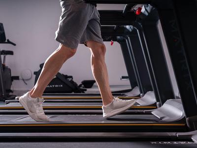 Person läuft auf einem Laufband in einem Fitnessstudio mit neutralem Hintergrund.