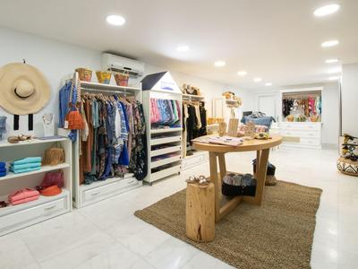 Hell beleuchteter, moderner Einzelhandelsraum mit Kleidung und Accessoires auf weißen Wänden und leichtem Boden.