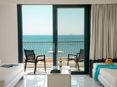 Helle Hotellounge mit Meerblick und Balkon mit Stühlen und kleinem Tisch.