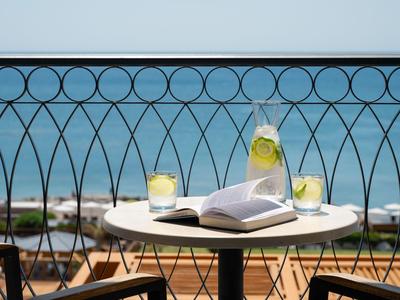 Balkon mit Tisch, offenem Buch, zwei Gläsern mit Getränken und Blick auf das Meer.