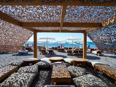 Vista da un'area lounge ombreggiata con cuscini verso la spiaggia e il mare in una giornata di sole