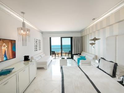 Modernes Hotelzimmer mit Meerblick, zwei Betten und Balkon mit Sitzgelegenheiten.