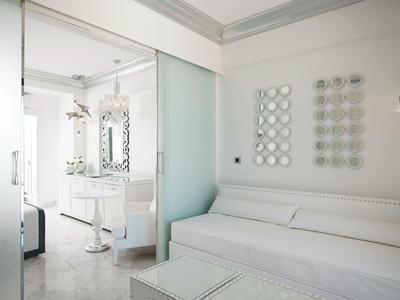 Modernes, weißes Hotelzimmer mit Sofa, Glastür und funktionalem Badezimmer.