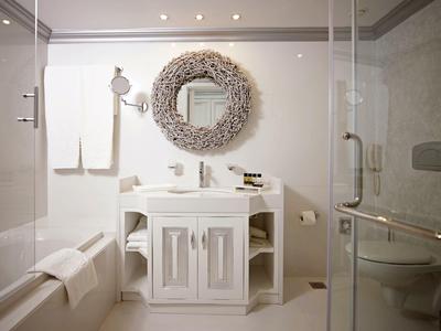 Modernes Badezimmer mit weißem Waschbecken, rundem Spiegel und Glastür zur Dusche.