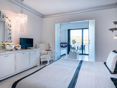 Modern eingerichtetes Hotelzimmer mit Doppelbett, TV und Zugang zu einem Balkon mit Meerblick.