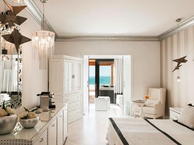 Helles Hotelzimmer mit großem Bett, weißer Einrichtung und Blick auf das Meer.