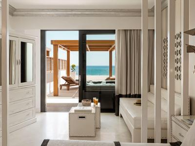 Modernes Hotelzimmer mit Blick auf das Meer durch große Glasfenster und Zugang zu einer Terrasse.
