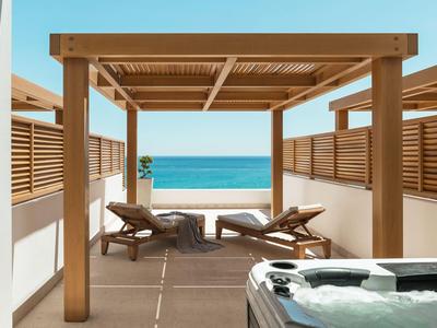 Ein Holzpergola mit Liegestühlen und einem Whirlpool mit Blick auf das Meer im Hotelgarten.