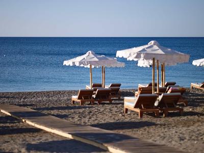 Spiaggia sabbiosa con più lettini e ombrelloni bianchi vicino a un mare calmo sotto un cielo sereno