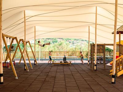 Große, überdachte Freizeitanlage mit Spielfläche und Spielgeräten im Außenbereich eines Hotels.