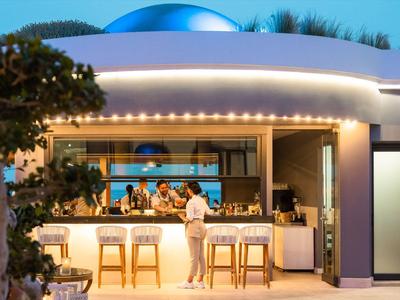 Außenbar eines Hotels mit leuchtender Theke und Gästen bei Abendlicht.