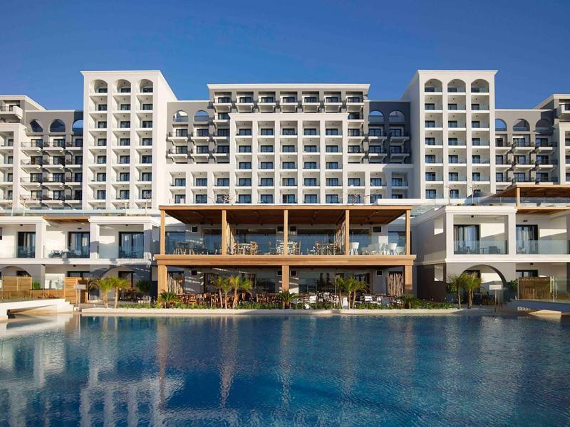 Grande hotel con più balconi e una piscina in primo piano sotto un cielo limpido.