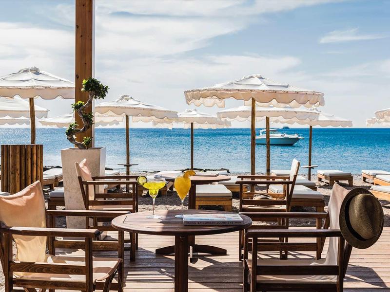 Terrazza soleggiata con sedie, tavoli e ombrelloni all'aperto vicino al mare.