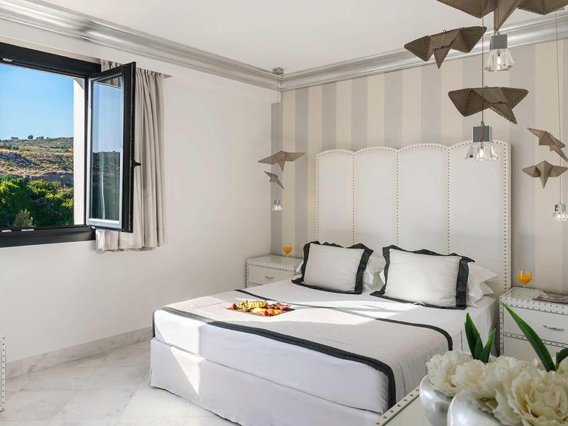 Camera luminosa con letto bianco, finestra con vista sulle montagne, arredamento minimalista e uccelli decorativi.