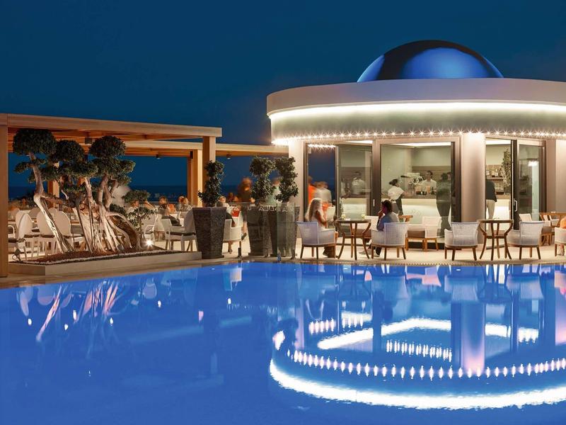 Terrazza dell'hotel di notte con piscina illuminata e ospiti che si rilassano.