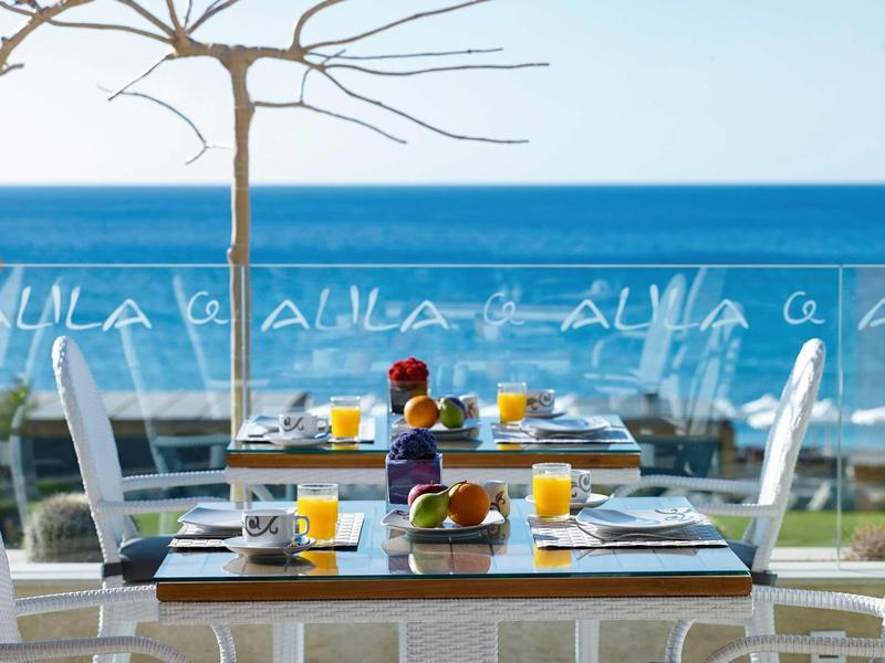 Tavolo per la colazione con succo d'arancia, caffè e croissant su balcone con vista mare.