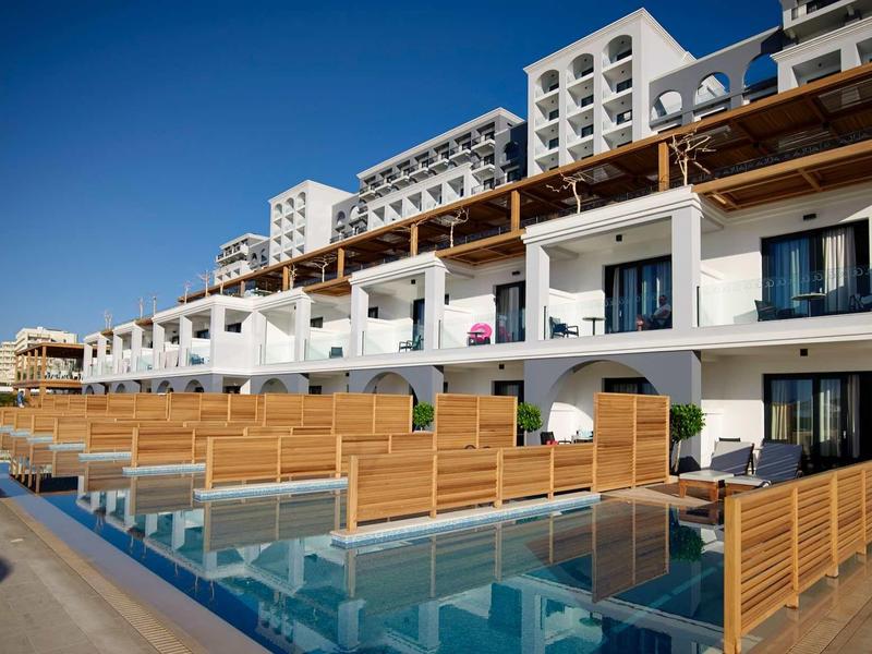 Complesso alberghiero moderno con terrazze, accesso diretto alla piscina e cielo sereno.