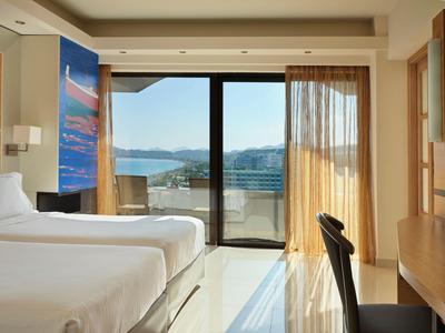 Camera d'hotel luminosa con due letti e balcone con vista mare e montagne.