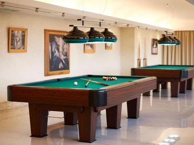 Sala giochi moderna con due tavoli da biliardo e lampade a sospensione, pareti bianche e design minimalista.