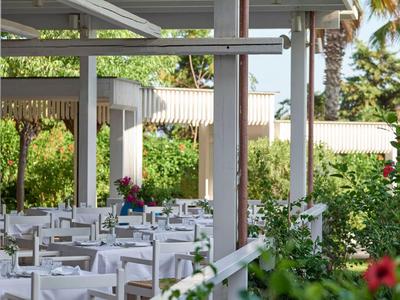 Terrazza esterna di un ristorante con tavoli e sedie bianche sotto un pergolato