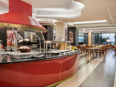 Area colazione moderna con buffet rosso e posti a sedere in un ristorante luminoso.