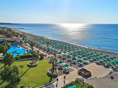 Spiaggia con ombrelloni verdi, piscina e mare sotto un cielo limpido.