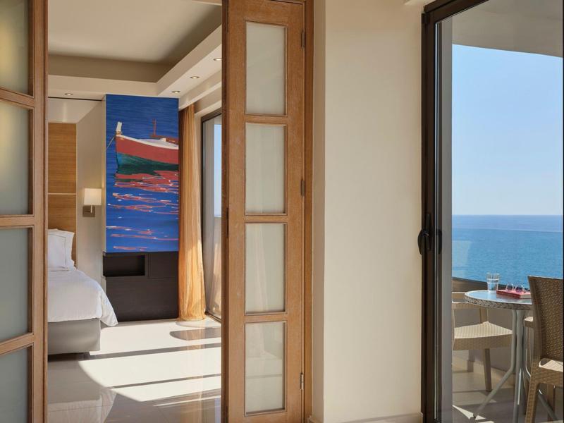 Luminoso atrio d'hotel con area salotto e vista sull'oceano attraverso grandi finestre.