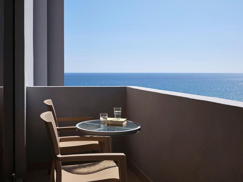 Balcone con tavolo, sedia e vista sul mare azzurro in una giornata di sole.