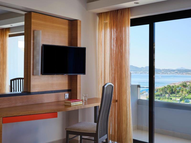 Camera d'hotel moderna con scrivania, sedia e balcone con vista sul mare.