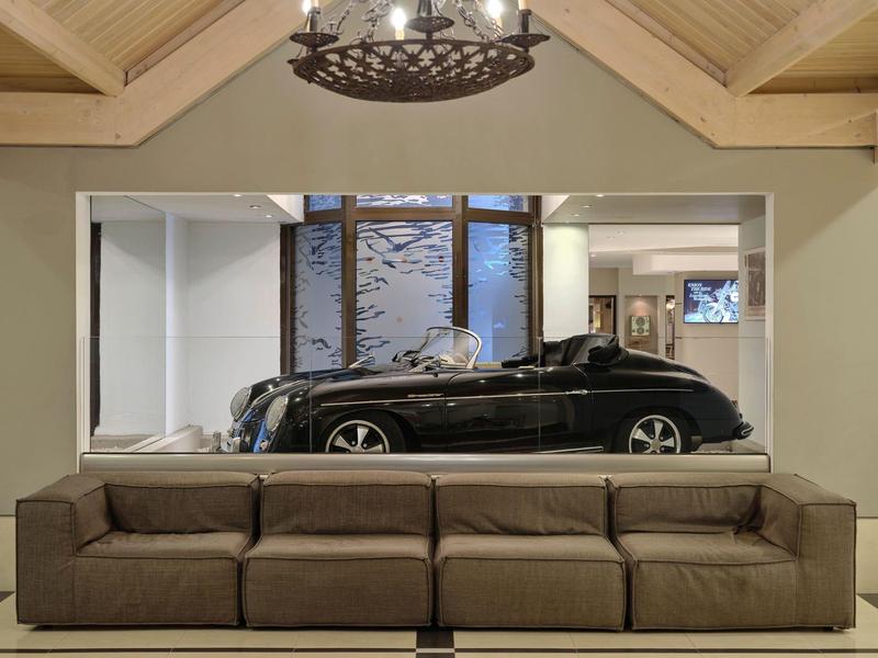 Divano marrone moderno davanti a uno specchio che riflette un'auto di lusso nera.