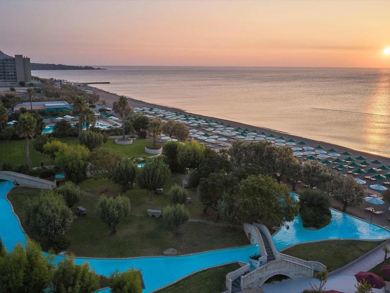 Vista sulla spiaggia al tramonto con lettini e piscina nel giardino dell'hotel.