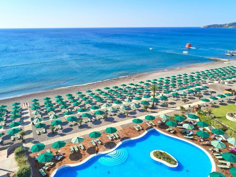 Vista di una spiaggia con ombrelloni verdi e una grande piscina dell'hotel.