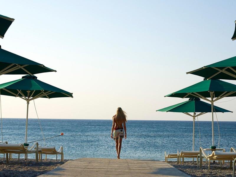 Donna cammina verso il mare tra ombrelloni su una spiaggia tranquilla.