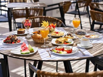 Round table set with breakfast dishes including fruit, eggs, coffee, and orange juice outdoors.